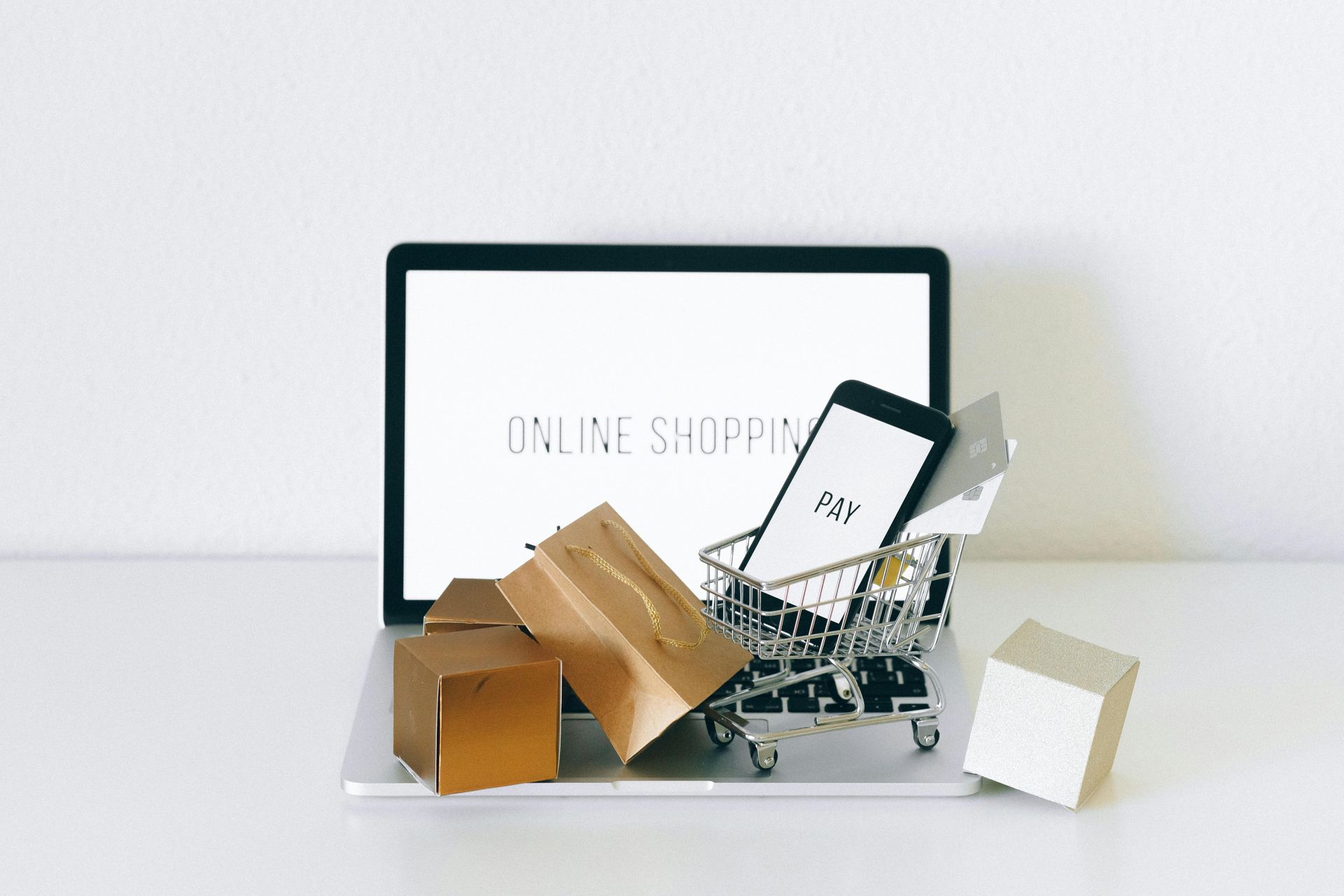 A laptop computer with a shopping cart filled with shopping bags , boxes , and a cell phone.