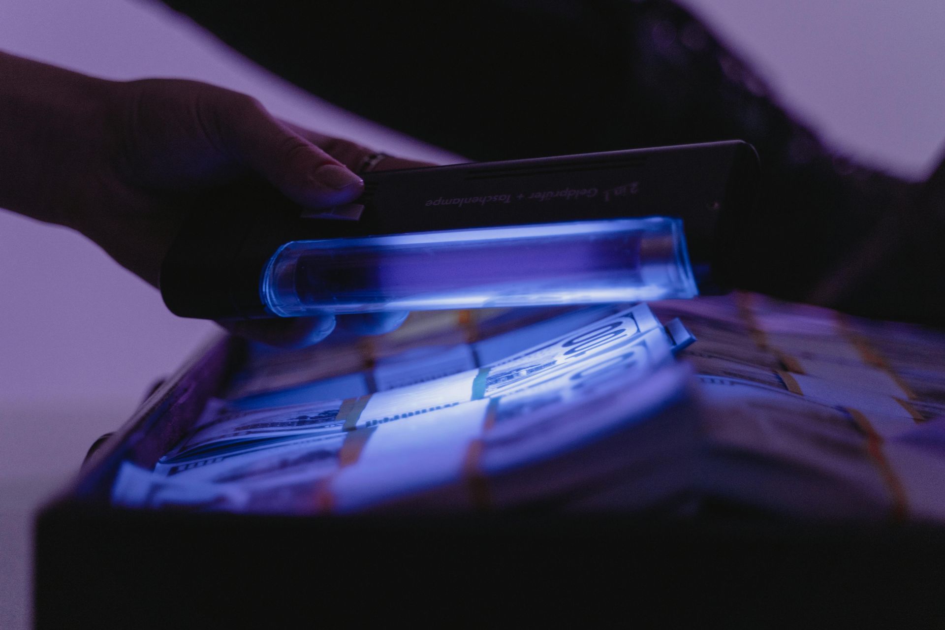 A person is holding a uv light over a pile of money.