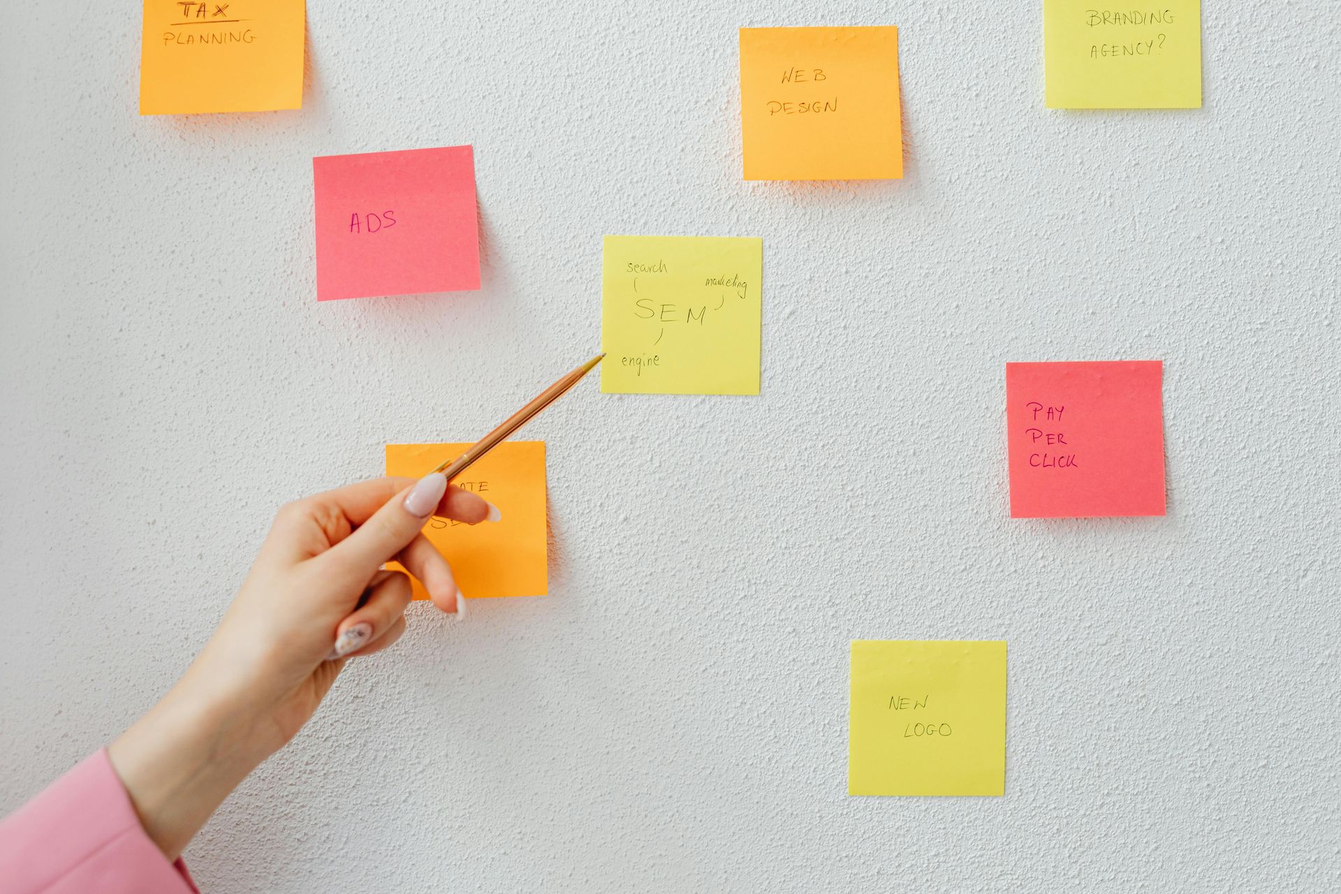 A person is pointing at a bunch of sticky notes on a wall.