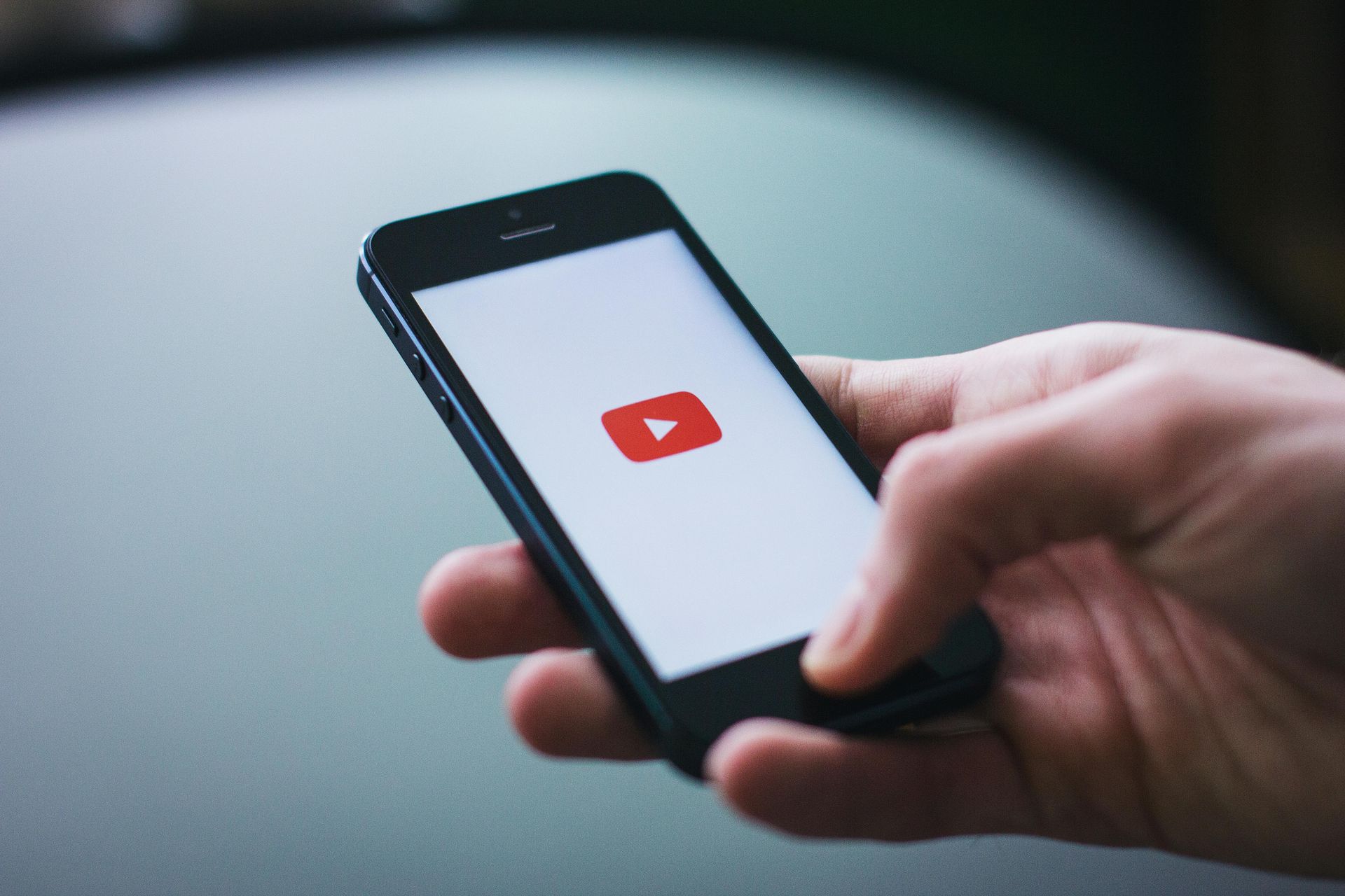 A person is holding a cell phone with a youtube logo on the screen.