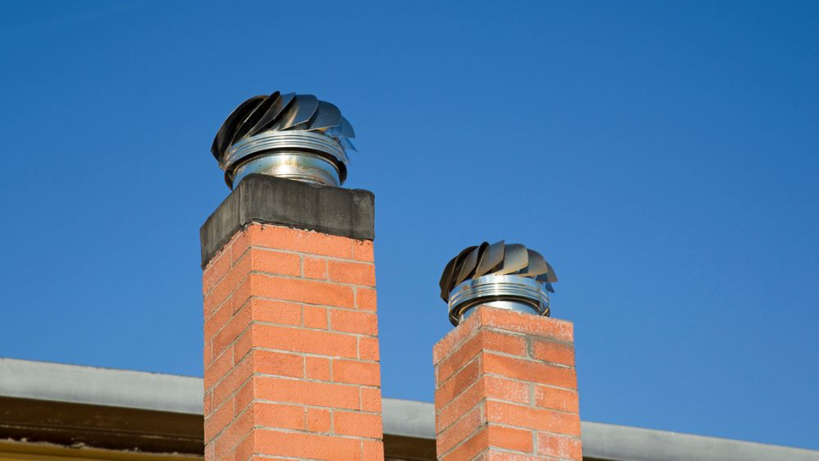 Two brick chimneys with spinning metal chimney caps against a clear blue sky.