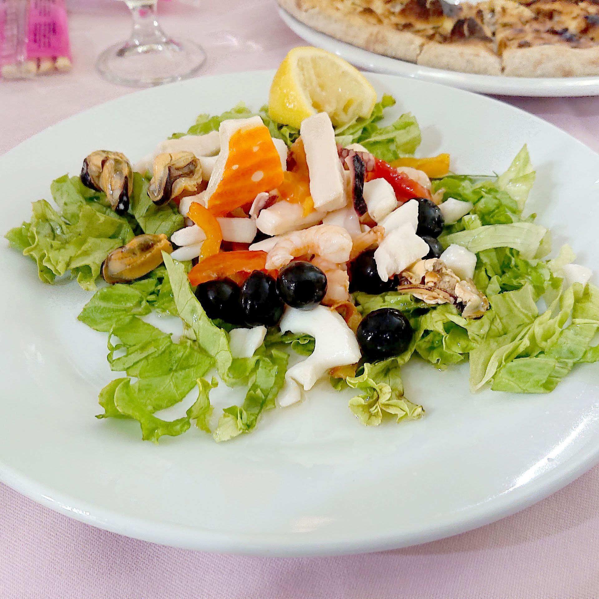 Insalata mista con lattuga, olive, funghi, formaggio, pomodoro e limone su un piatto bianco