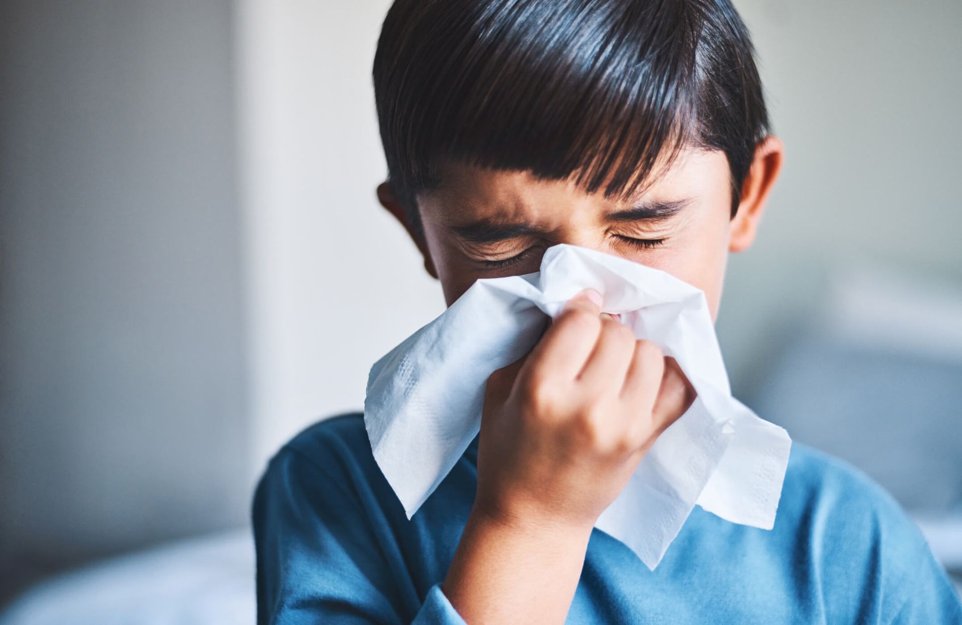 Person in a blue shirt blowing their nose into a tissue, close-up.