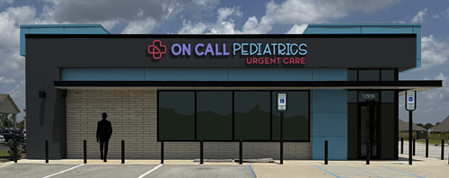 Exterior of On Call Pediatrics storefront with teal sign, dark facade, windows, and parking spaces in front
