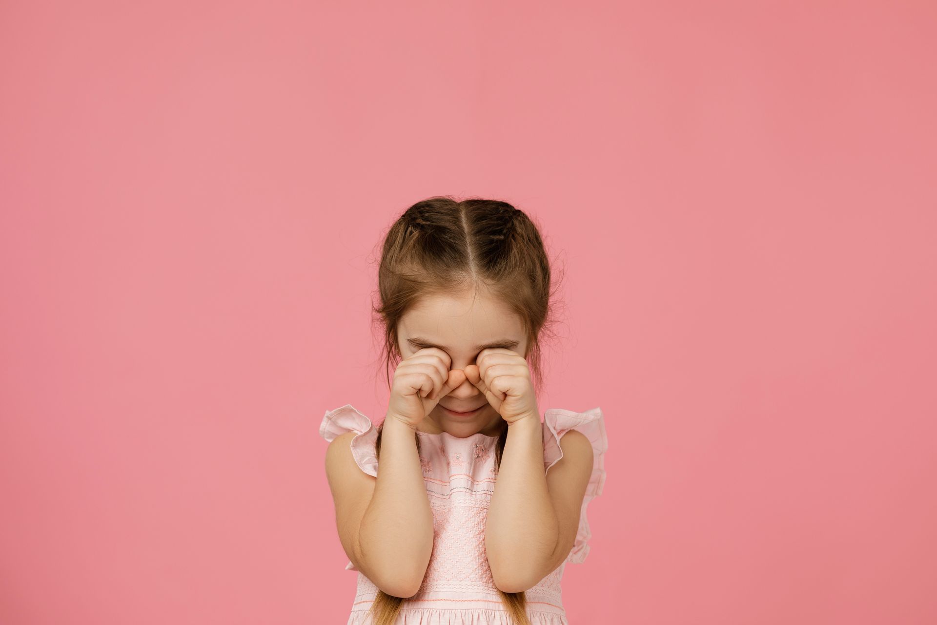 Child rubbing eyes against pink background