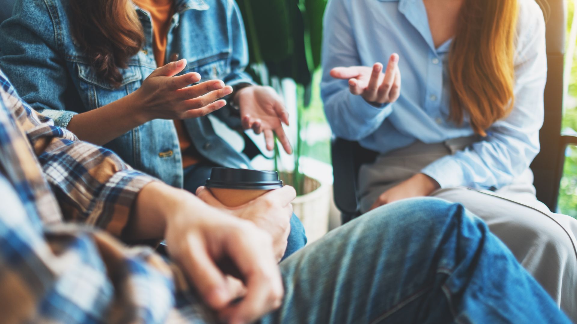 Three people sit in a group, engaged in a conversation with their hands gesturing.