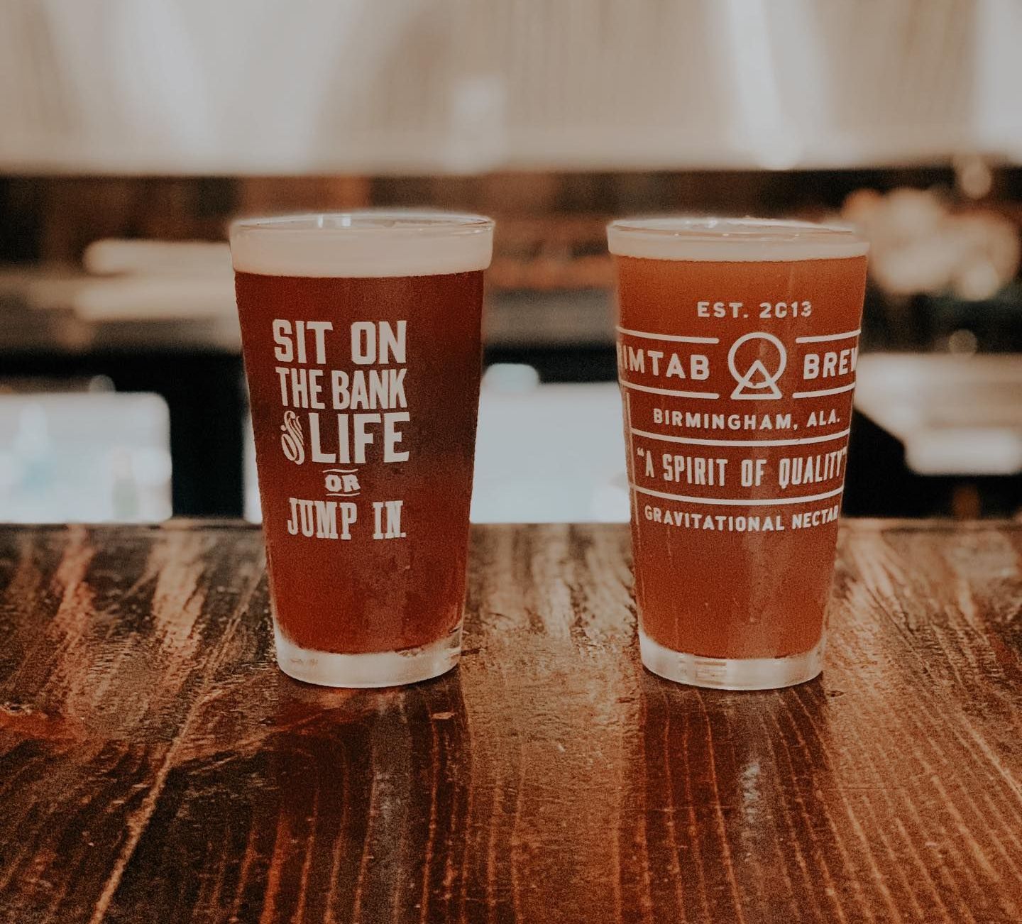 Two glasses of beer are sitting on a wooden table.