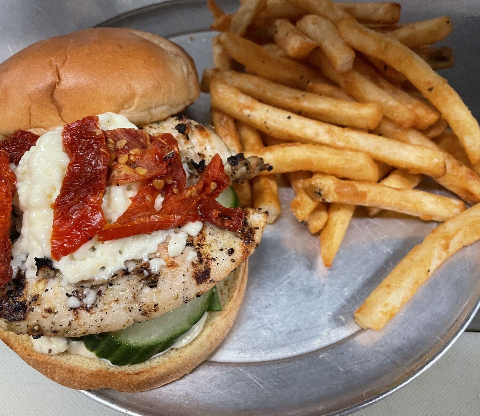 A person is holding a hamburger in front of a plate of french fries.