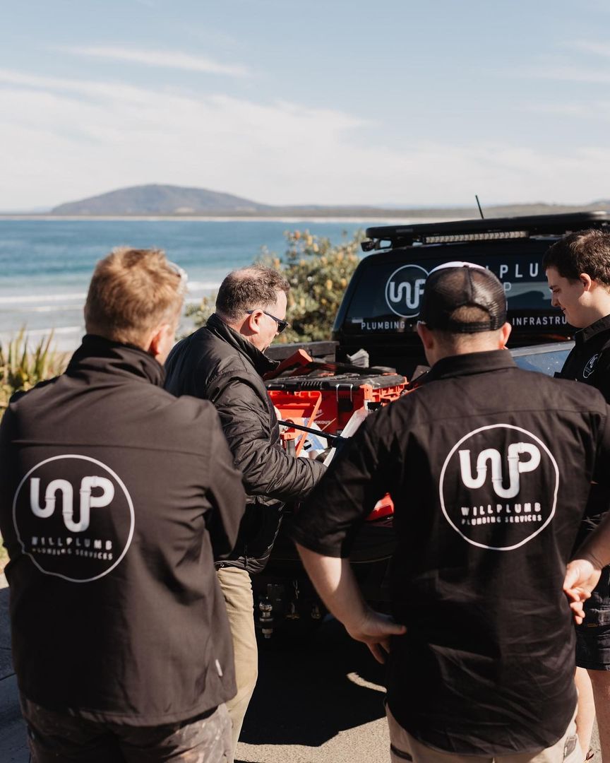 Four people wearing company branded clothing work on equipment in the back of a truck near a beach.