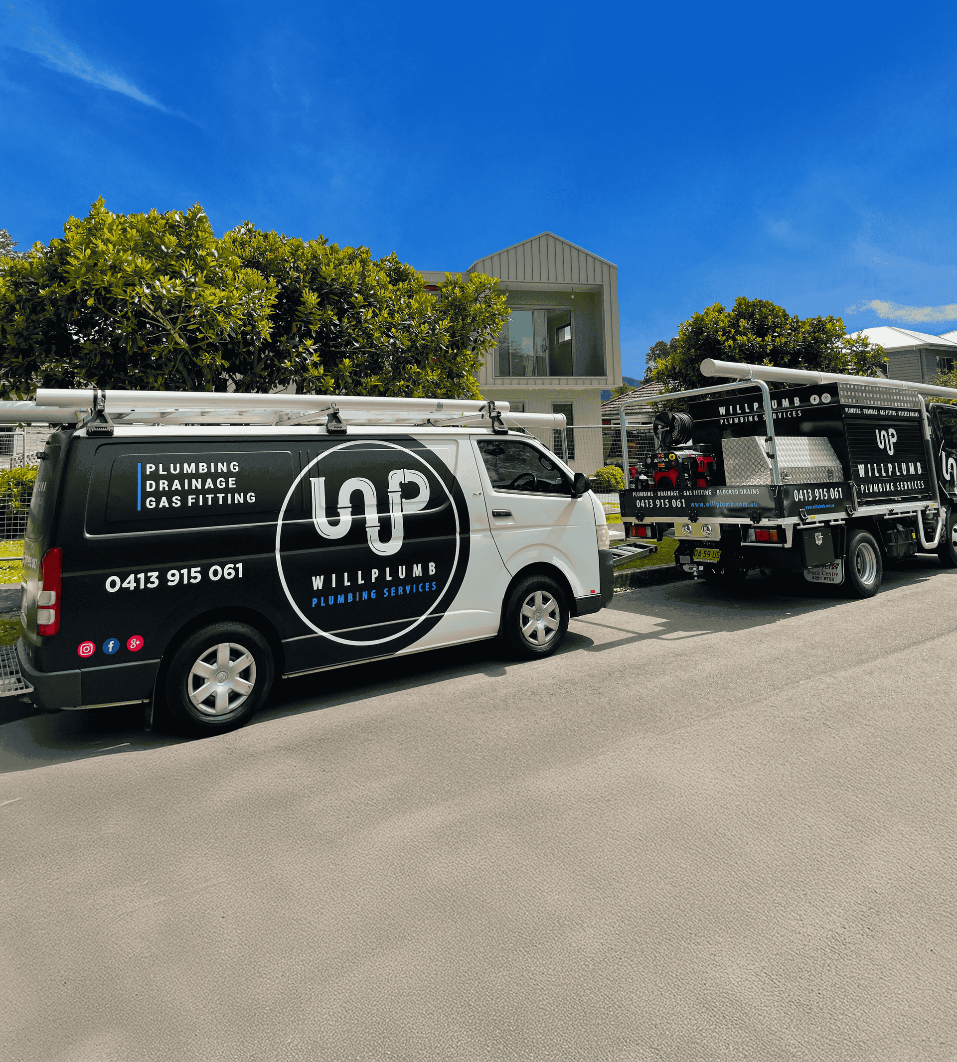 Two black and white work vans parked on a paved driveway in front of a modern house under a bright blue sky.