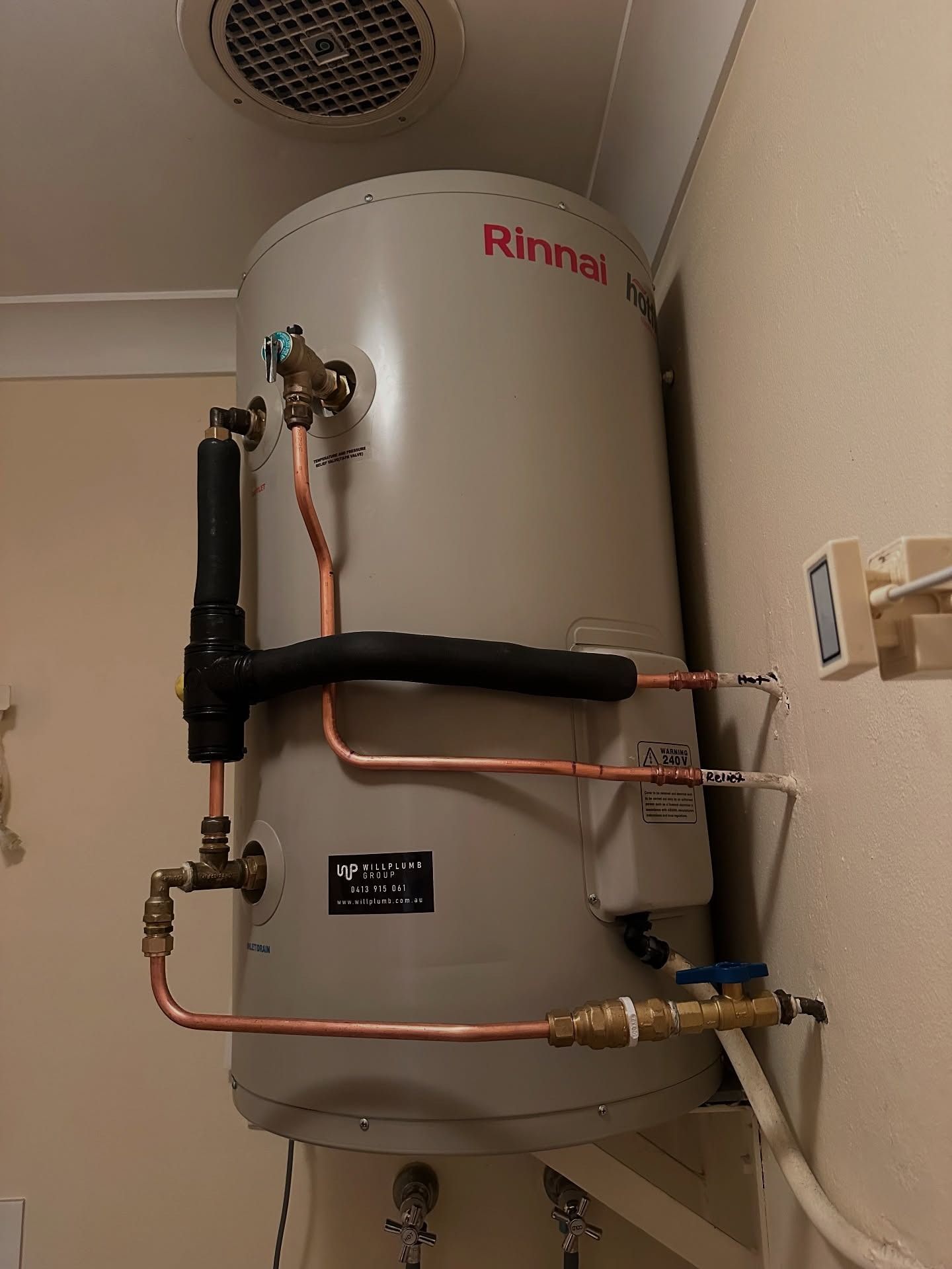 A wall-mounted Rinnai hot water cylinder with copper plumbing pipes in an indoor setting.