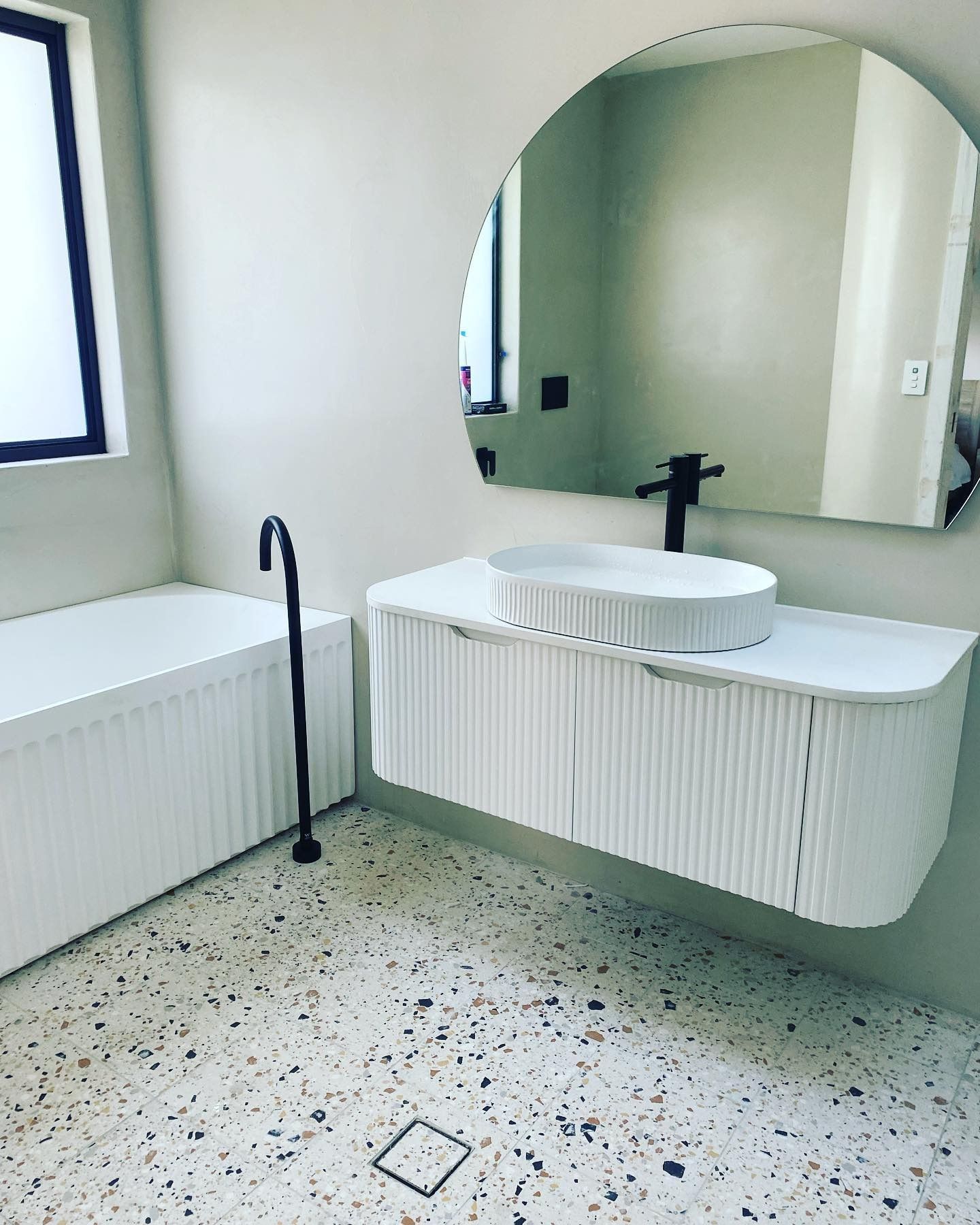 A modern bathroom with a white fluted vanity, a vessel sink, a matte black faucet, and speckled flooring.