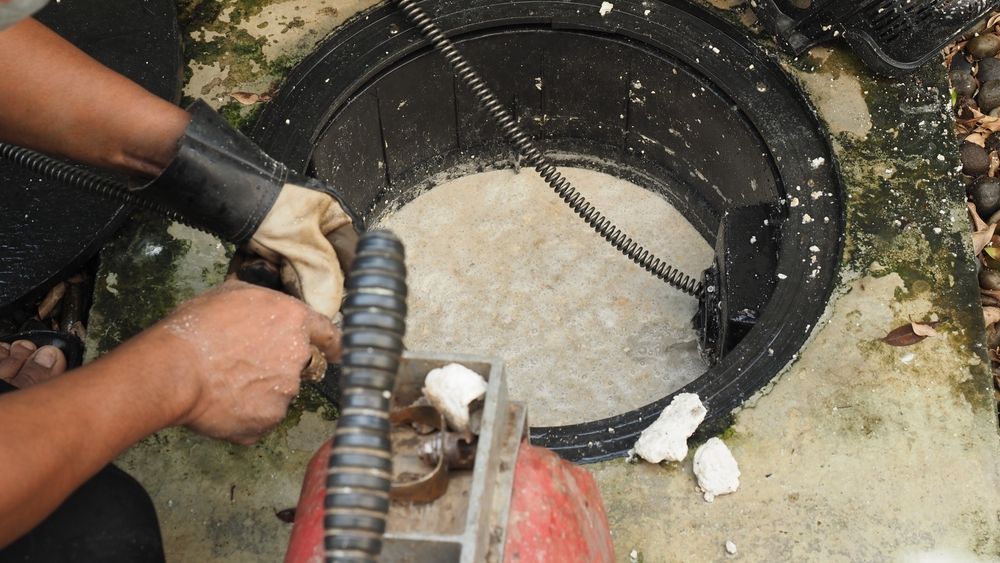 An open, rectangular outdoor drain filled with dark, stagnant water and accumulated debris, sludge, and organic matter.