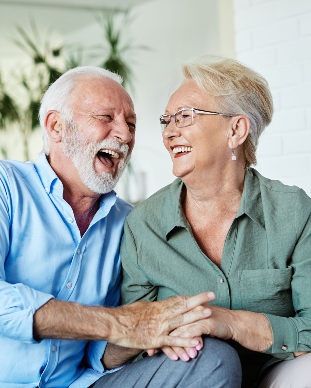 Two people laughing while holding hands and sitting together in a brightly lit indoor space.