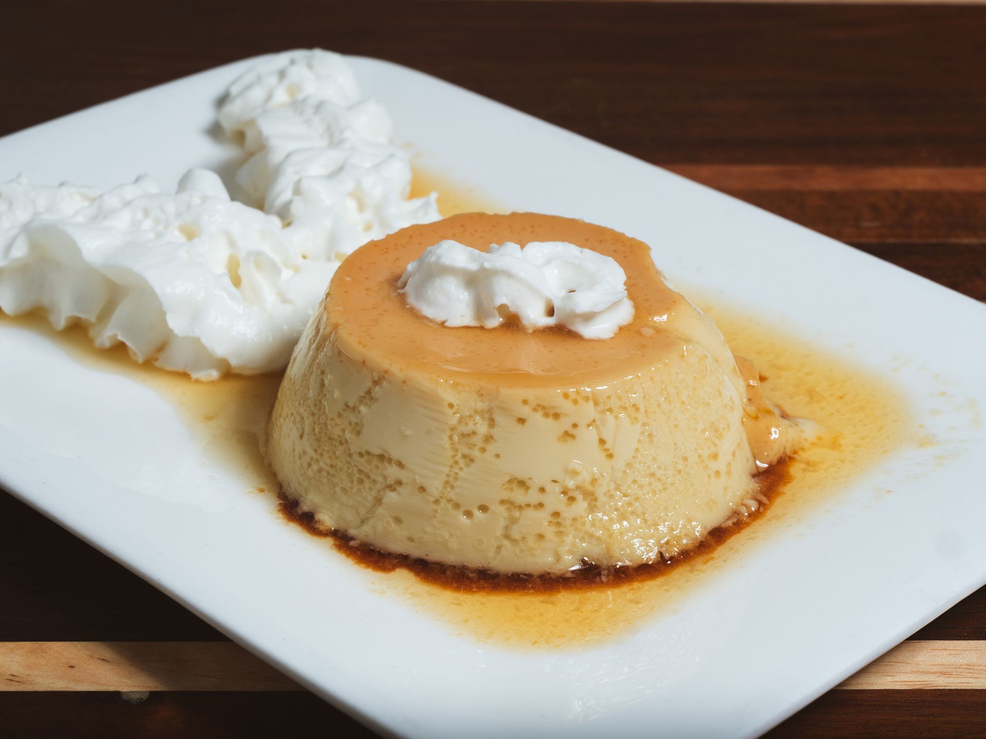 Flan dessert with caramel sauce and whipped cream on a white plate.