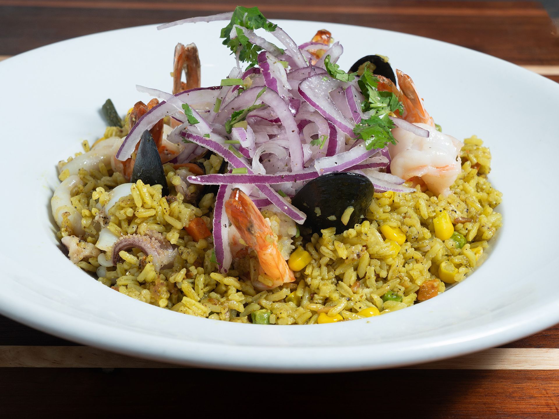 Seafood rice dish: yellow rice, shrimp, mussels, red onions, and cilantro in a white bowl.