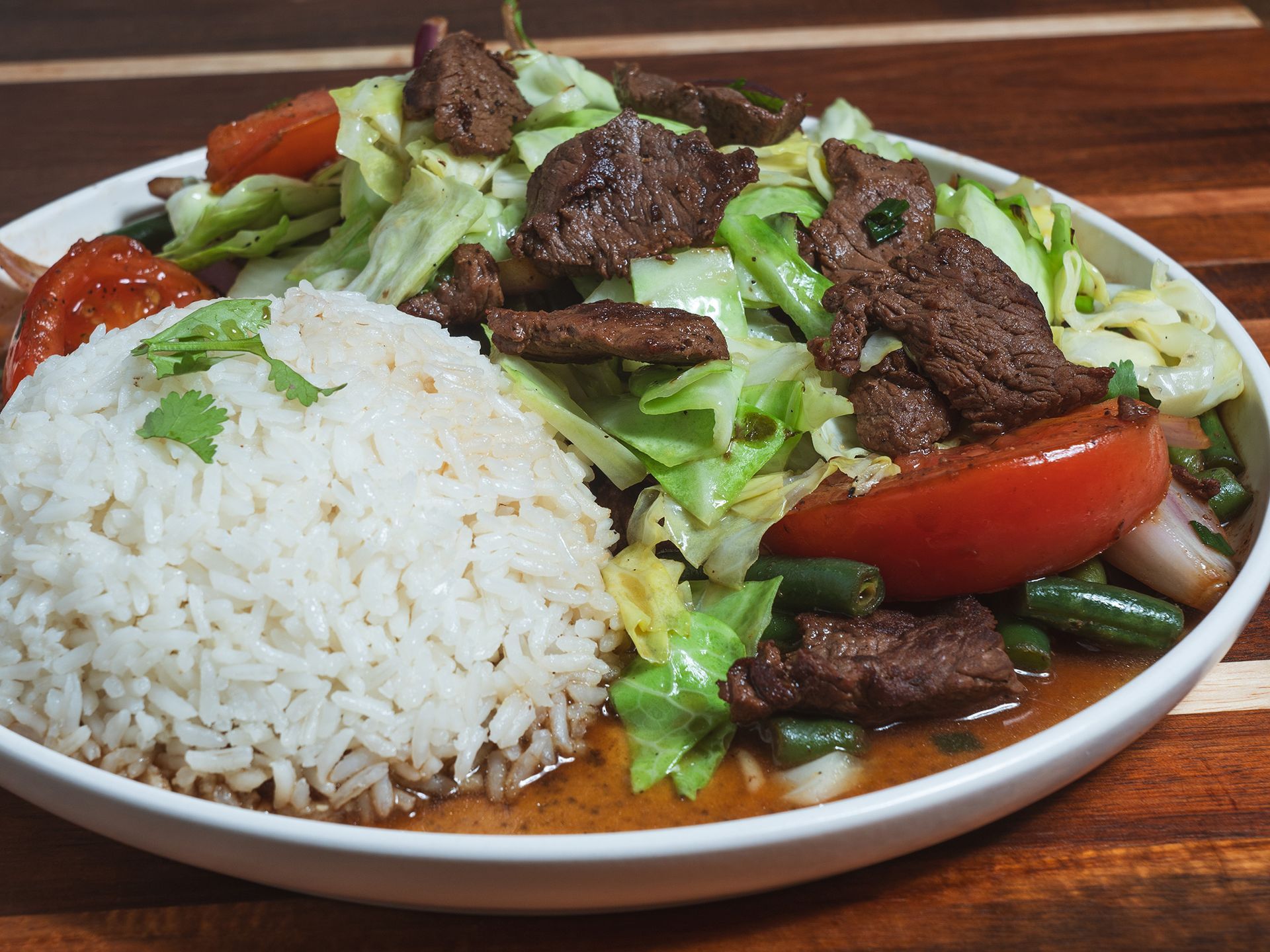 Beef stir-fry with rice, tomatoes, green beans, and cabbage on a white plate.