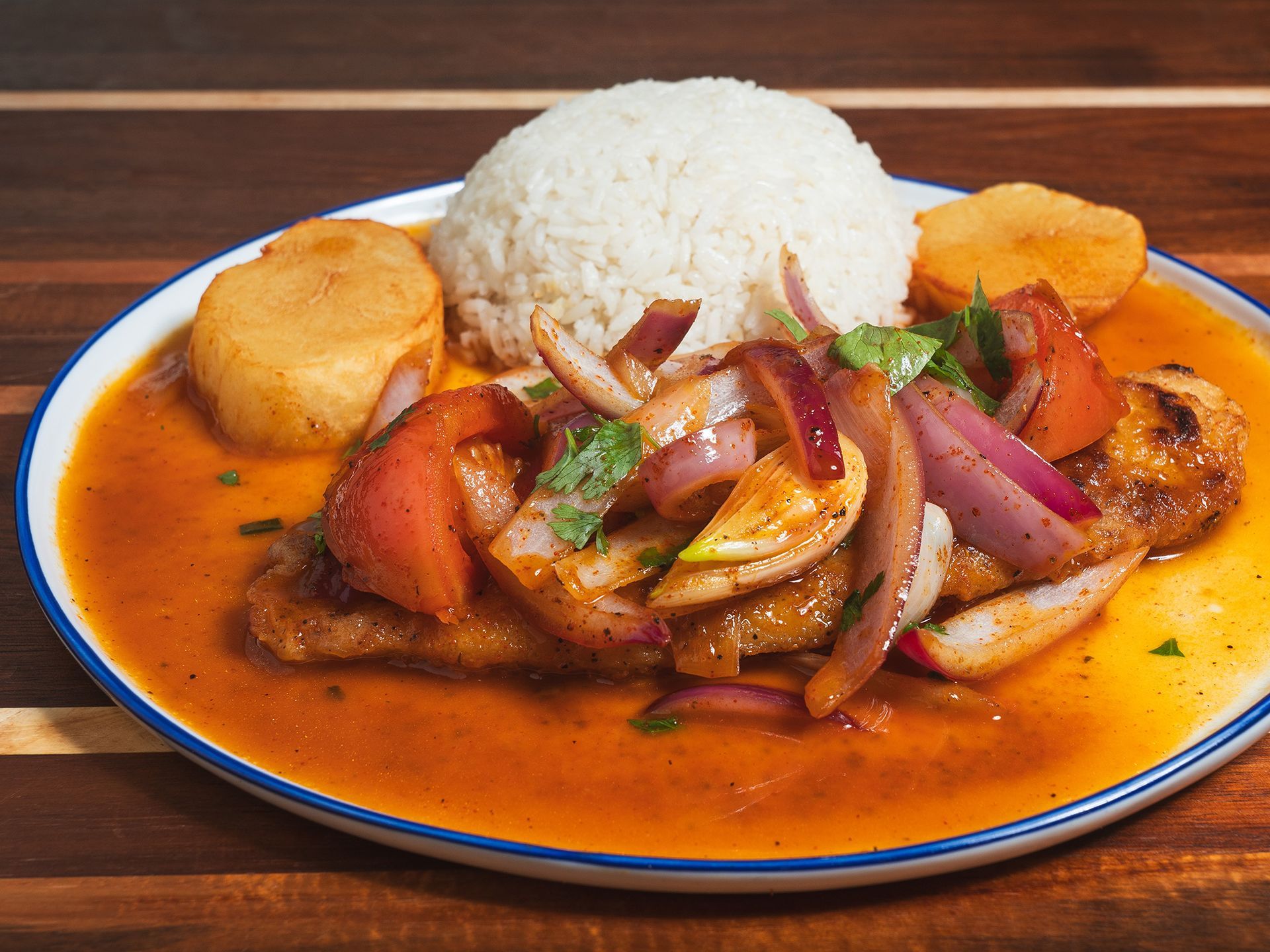 Peruvian dish: breaded fish in sauce, topped with onions, tomatoes, and cilantro, served with rice and potatoes.