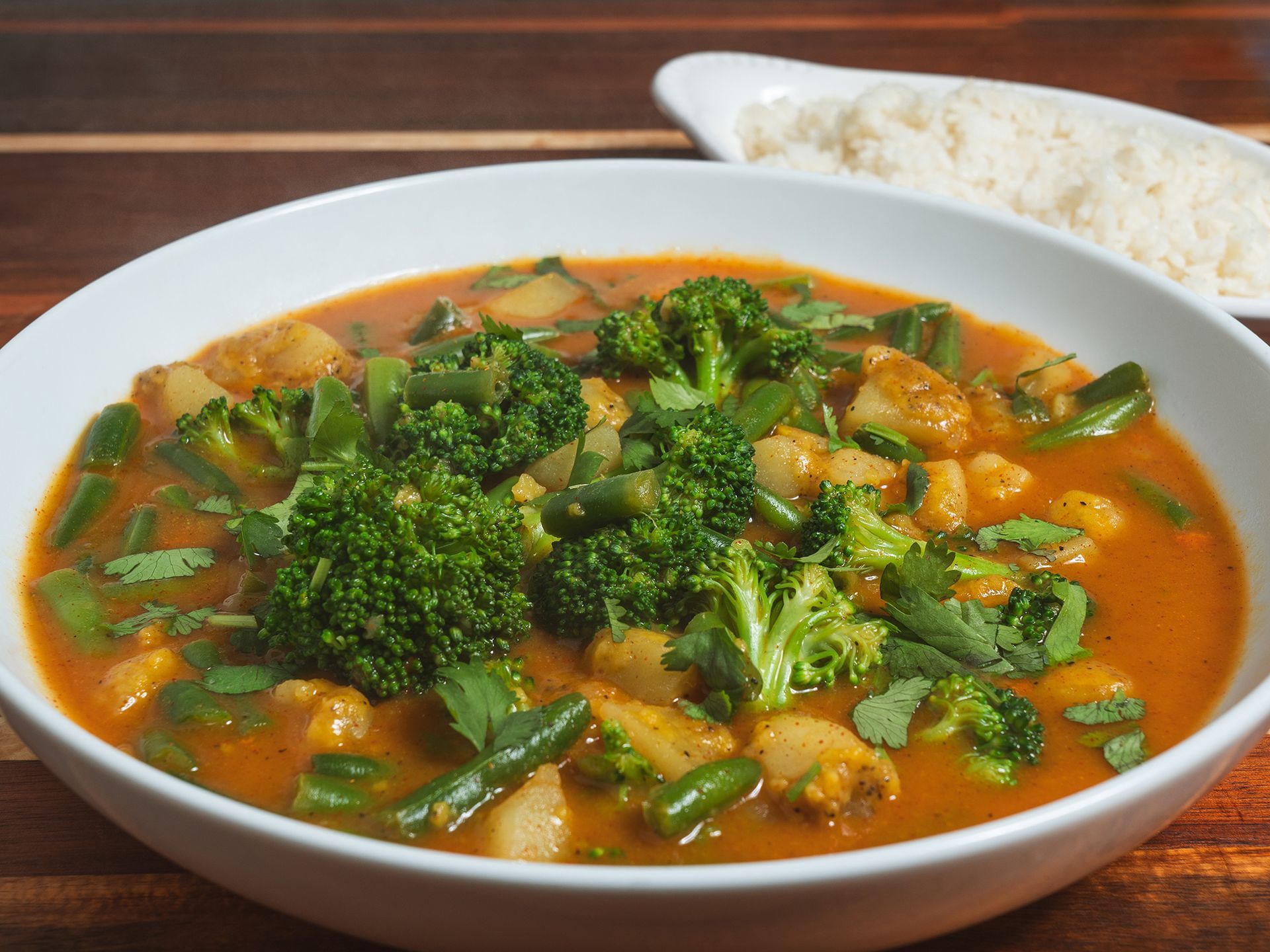 Vegetable curry with broccoli and green beans in a white bowl, served with rice.
