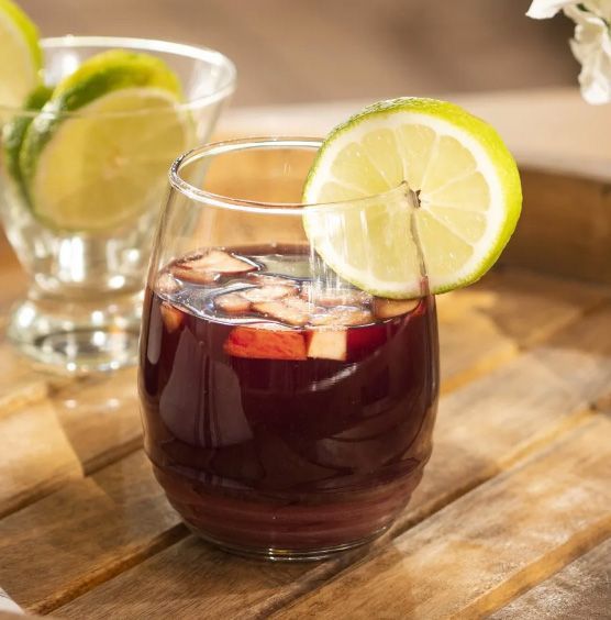 Sangria in a glass with lemon slice, apple pieces, on a wooden surface.