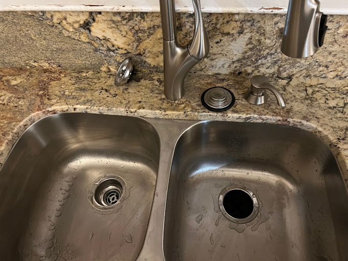A stainless steel kitchen sink with a faucet on a granite counter top.