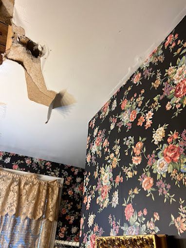 A room with floral wallpaper and a ceiling with a hole in it.