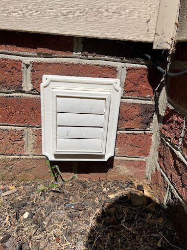 A white vent is sitting on the side of a brick wall.