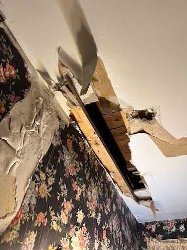 A room with a hole in the ceiling and a floral wallpaper.