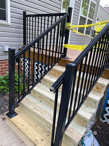 A wooden deck with a black railing is being built next to a house.