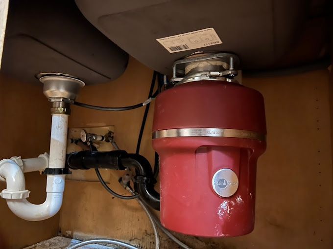 A red garbage disposal is under a sink in a kitchen