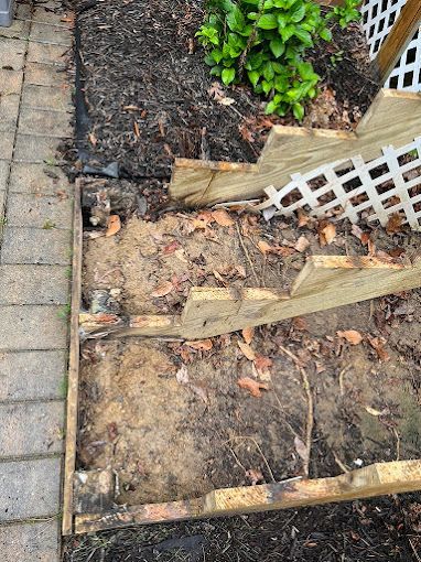 A wooden fence is sitting in the dirt next to a brick walkway.
