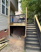 A wooden deck with stairs leading up to it is being built next to a house.