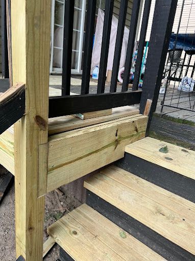 A close up of a wooden deck with stairs and a black railing.