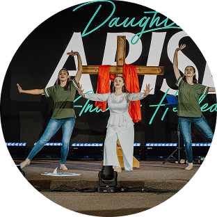 Three people posing on stage with arms raised in front of a large colorful sign.