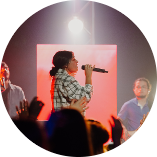 Singer performing on a lit stage, holding a microphone before a cheering crowd.