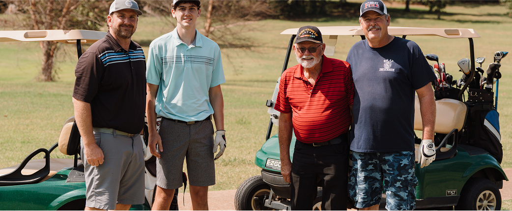 Four people posing beside a golf cart on a sunny outdoor course
