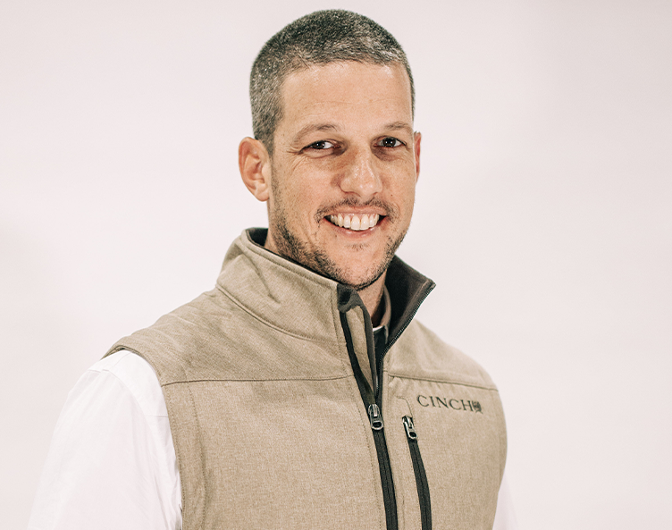 Smiling person in a beige vest over a white shirt against a light background