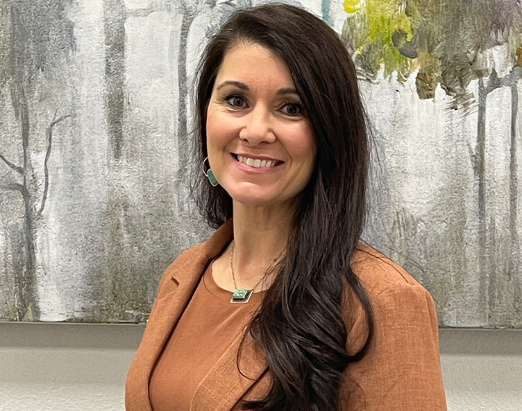 Smiling woman in a rust top standing before an abstract gray and gold painting
