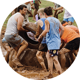 People carrying a mud-covered tire through a muddy obstacle course