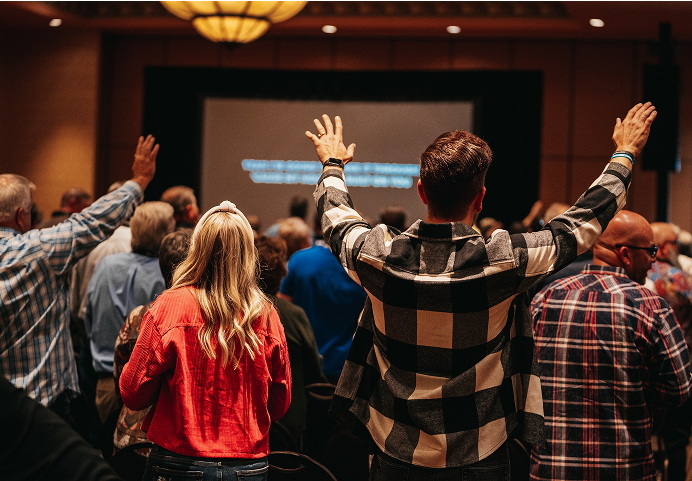 Audience with raised hands during a presentation in a dim conference room