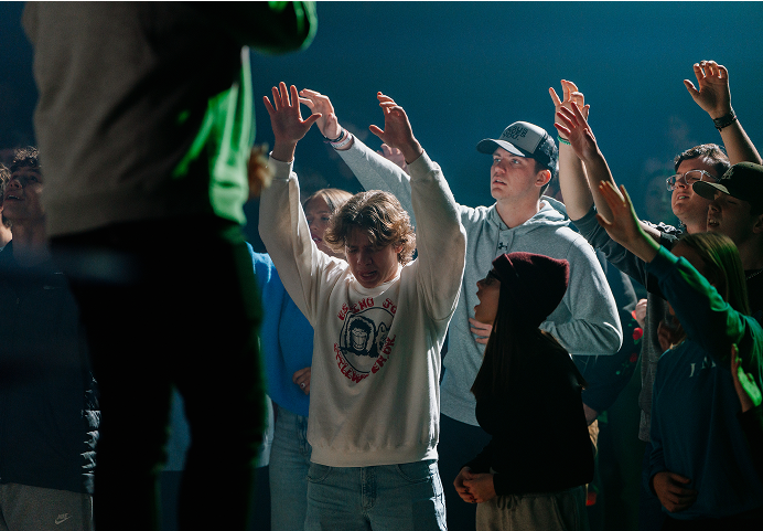 People raising hands in a crowd at an outdoor event under dramatic lighting