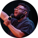 Singer holding a microphone and singing onstage under dark lighting