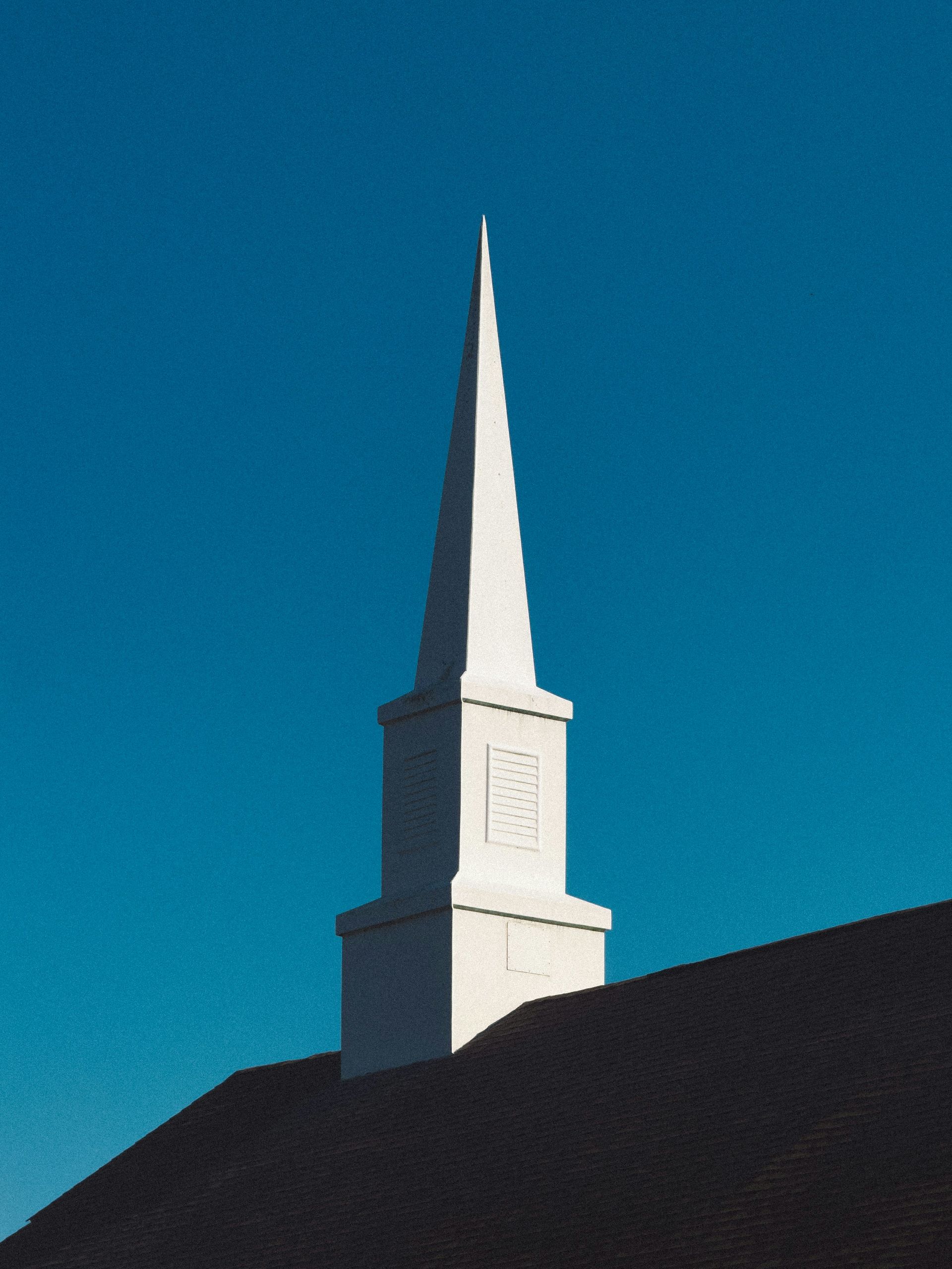 White church steeple on a dark hill against a clear blue sky