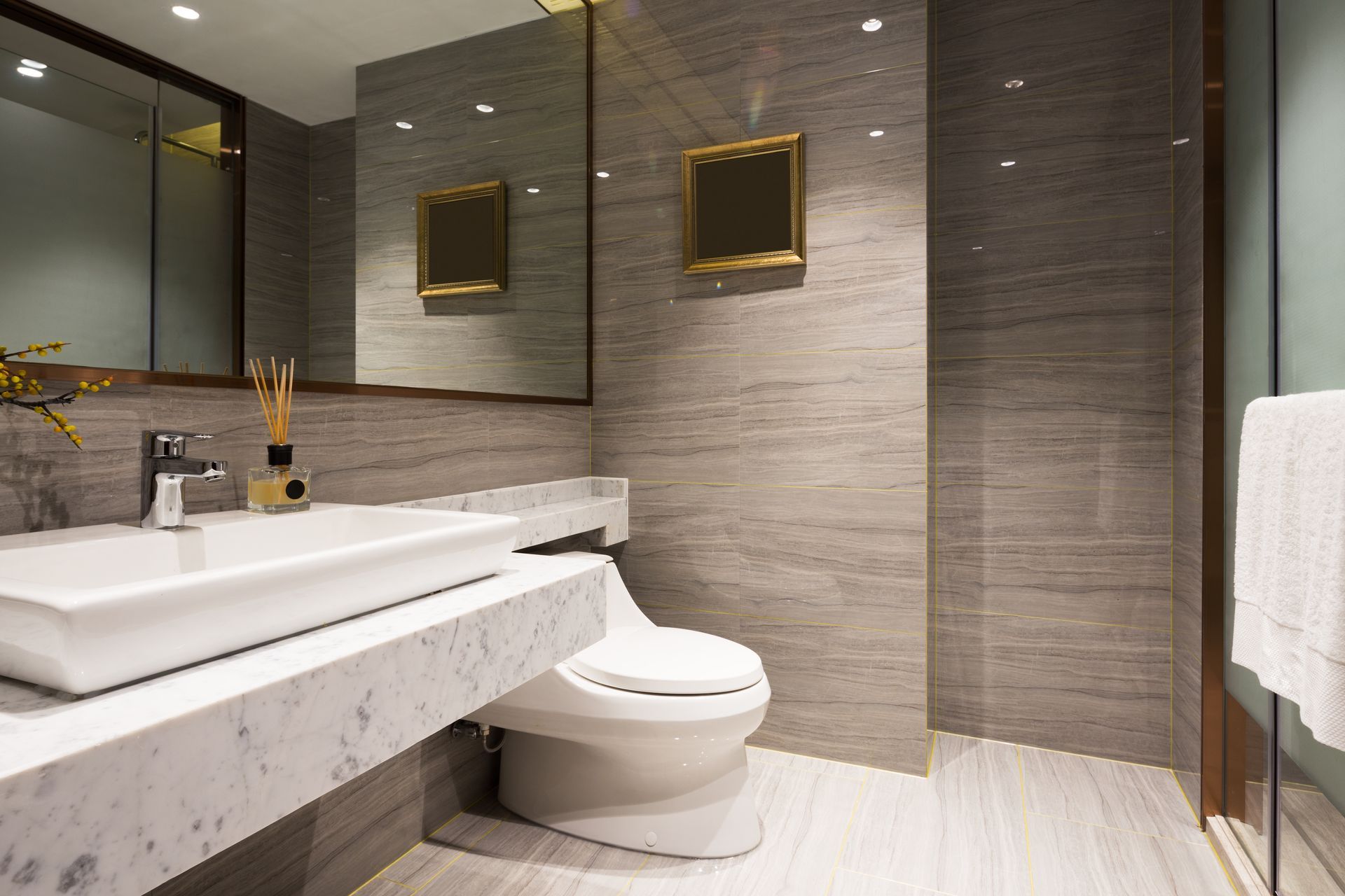 Modern bathroom with marble vanity, wall-mounted sink, toilet, and large mirror panels