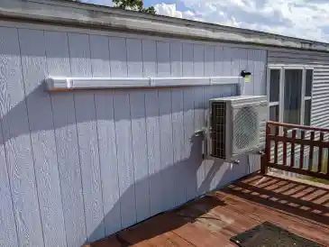 Exterior wall with a mounted air conditioner and white trim above a wooden deck.
