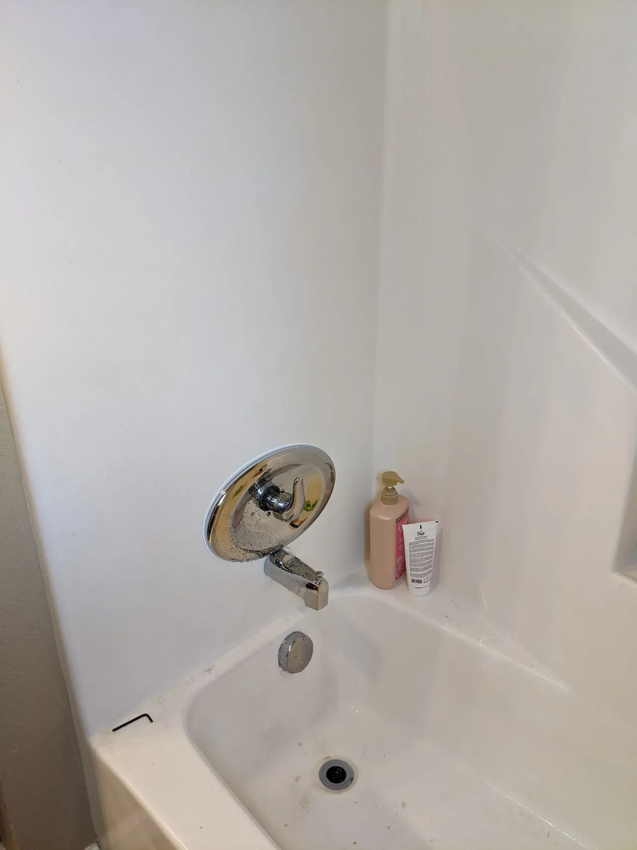 Bathroom sink and bathtub corner with handheld mirror and toiletries on the ledge