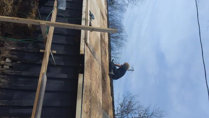 Person on a rooftop beside wooden framing under a cloudy sky