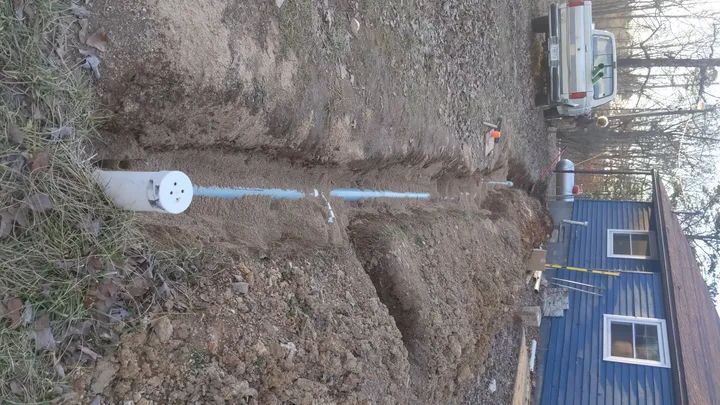 Backyard trench with a blue pipe and white cap beside a house and parked SUV