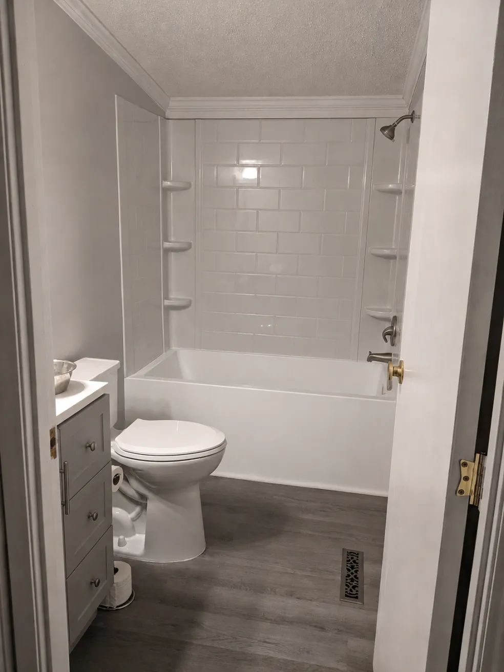 Small bathroom with a toilet, vanity, white tub surround, and gray floor