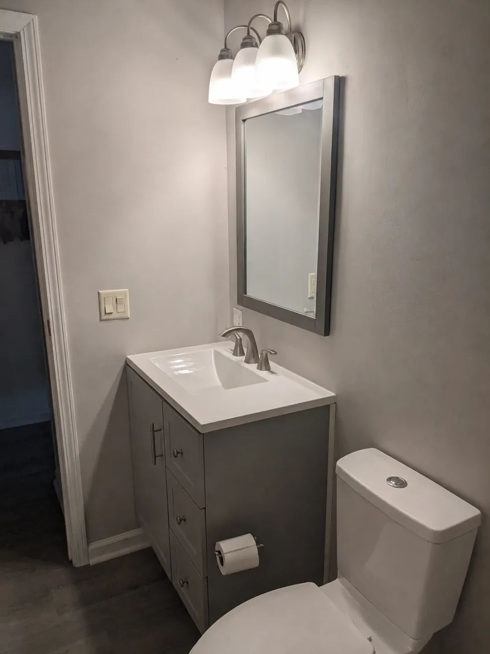 Small bathroom with vanity, mirror, light fixture, and toilet in gray and white.